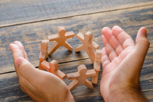 Wooden figures of people forming a circle, held gently in cupped hands, symbolizing frictionless membership