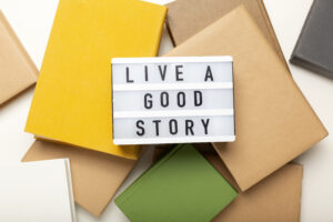 Lightbox sign reading "Live a good story" resting on a pile of colorful books, illustrating