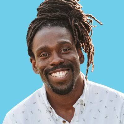 Cam Awesome, motivational speaker and former amateur boxer, smiling against a blue background.