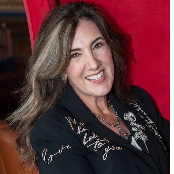 Motivational speaker Christine Cashen smiling in a black jacket against a red background.
