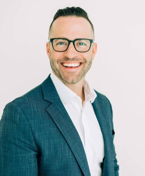Jake Thompson, international keynote speaker and leadership performance coach, wearing a blue blazer and glasses.