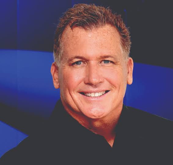 Motivational keynote speaker Scott Burrows smiling against a blue background.